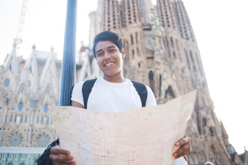 Half length portrait of cheerful Latin tourist with paper location map smiling at camera during...