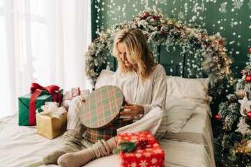 Obraz na płótnie Canvas Caucasian attractive blonde woman opens Christmas gift boxes while sitting on bed in the bedroom