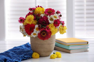 Beautiful bouquet and books on white wooden table near window