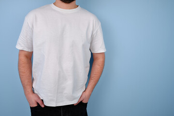 Man in a white T-shirt poses near a blue wall. Hand gestures and emotions. Studio photography. The concept of emotion, strength and fun. Casual wear. Space for inscriptions and logo