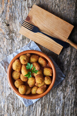 grupo de buñuelos de bacalao caseros en un bol de tierra sobre una mesa rustica de madera