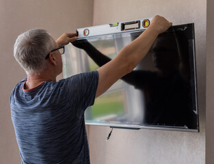 Side view of mature technician installing tv at home.