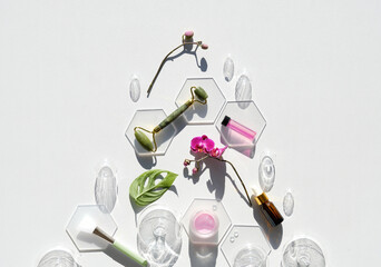 Jade stone face roller with monstera leaf, orchid flowers and glass baubles. Pink moisturizer cream...