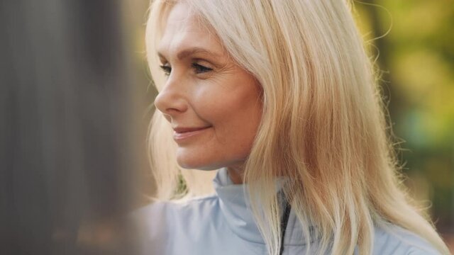 Cheerful blond mature woman listening her friends outdoors