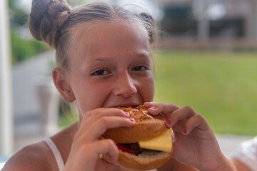 teen girl eating hamburgerand laughing on the balcony on a sunny day