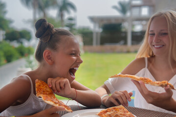 Two girls holding pizza and laughing on the balcony on a sunny day