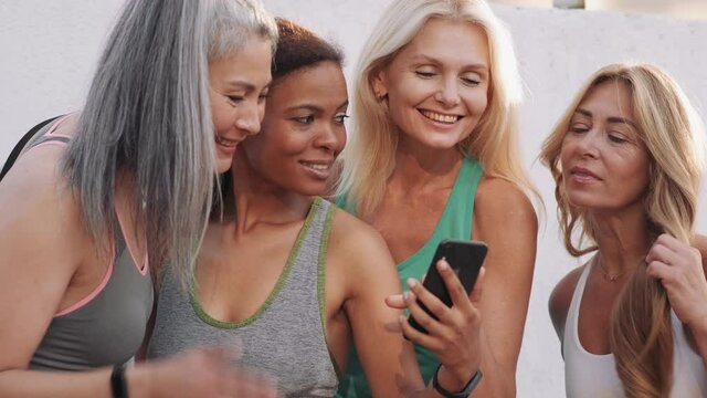 Smiling multinational adult women looking at the phone outdoors