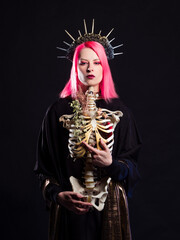 A Gothic queen in a crown with roses and rays holds a skeleton of a man without a head in her arms....