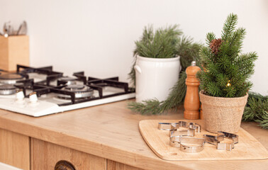 Christmas metal cookie molds on cutting board with little Christmas tree next to kitchen stove, baking background in bright decorated festive interior, space for text