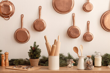 Christmas kitchen counter or table in bright modern festive cozy interior with New Year decorations, baking utensils, rolling pins, metal cookie molds, copper pans on wall and little Christmas tree
