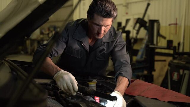 Auto mechanic man standing at the opened hood and lighting with lamp while working at the workshop and making chip tuning. Car service, repair and people concept