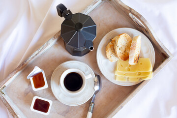 A fried toast, a coffee pot and a cup of black coffee without focus are on a wooden tray against the background of a white bed. View from the top point. Free space for text.