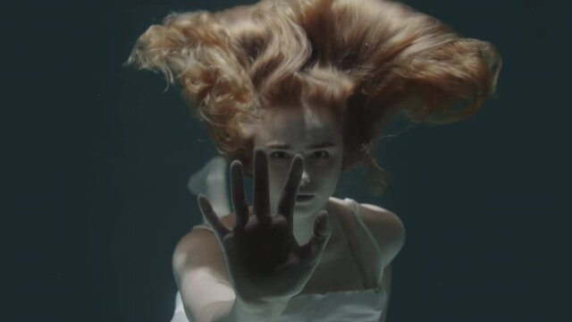beautiful red-haired girl stopped underwater in front of the camera and froze