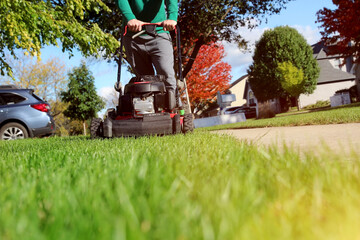 Mowing the grass with a lawn mower in sunny autumn. Gardener cuts the lawn in the garden.