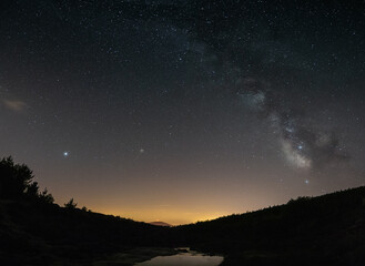 Fototapeta na wymiar Milky Way reflected in a lake on the top of the mountain and with the lights of Portugal behind