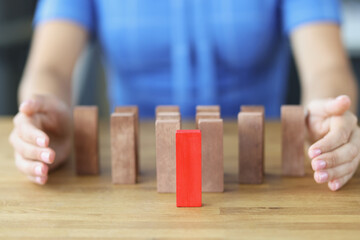 Red block standing on table in front of wooden ones near female hands closeup