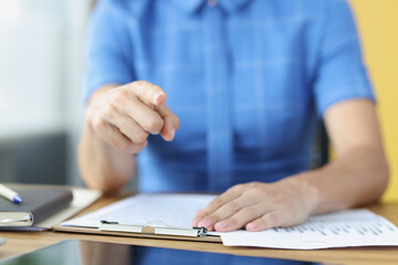 Woman sitting at table with documents and pointing finger closeup