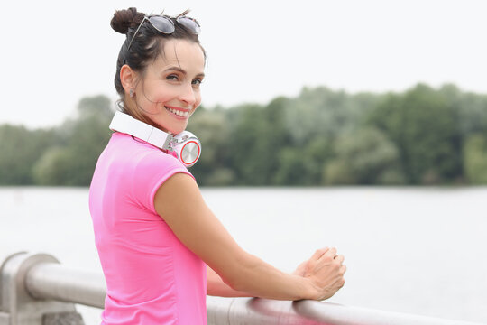 Young smiling woman with headphones on her neck standing on bridge