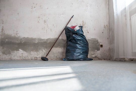 Renovierungsarbeiten: Besen und Müllsack mit Tapetenmüll vor einer nackten Wand