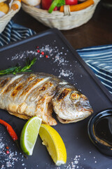 Grilled fish on a plate with a glass of wine and baked vegetables.