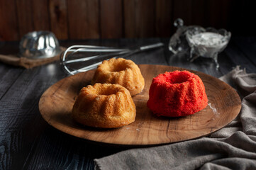 vanilla and red velvet puddings with powdered sugar with strainer and whisk on wooden table and plate and window light