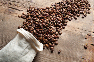 coffee beans are falling from a white sack on an old wooden background. Copy space