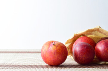 Close up, plums on tablecloth and inside kraft paper bag. Copy space.