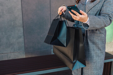 Girl with a phone in her hands and black shopping bags near a mall, black friday, sale time
