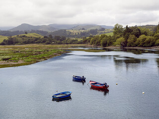Fototapeta premium Paisaje de San Vicente de la Barquera con tres barcas en el agua, y el reflejo de las nubes y montañas al fondo, en Cantabria, España, en el verano de 2020.