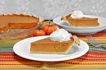 Pumpkin pie slice with whole pie in background.