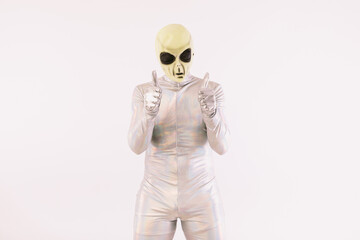 Person wearing silver suit and green alien mask with thumbs up, on white background