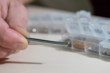 A close-up of male hands takes a screw for repairing glasses with tweezers
