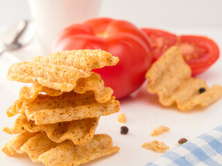 Whole Grain crisps with tomato salsa flavor on the white table and red tomatoes on the background.. Whole grain crisps.