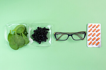 Top view of natural blueberries, spinach, vitamin capsules for improving vision and eye glasses on...