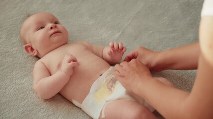 Mother changing diaper on her newborn baby. Mother changing diaper on her infant baby indoors.  Mom puts diapers on her newborn baby on a changing table.