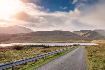 Small narrow asphalt road in beautiful nature setting. Road goes downhill into amazing mountains....
