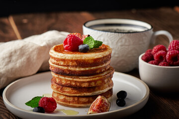Tasty appetizing homemade pancakes served with honey, raspberries and blueberries on plate on dark background