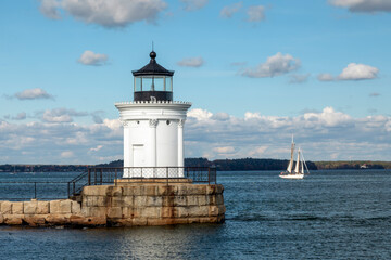 Fototapeta na wymiar Resembling a Greek monument with Corinthian columns, the Portland Breakwater Lighthouse, also called Bug Light, marks the harbor at Portland, Maine with a sailboat in the distance.