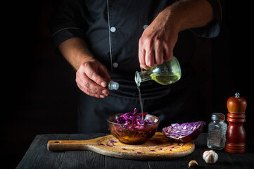 A professional chef pours olive oil into a fresh red cabbage salad. Cooking healthy food in restaurant kitchen on vintage table.