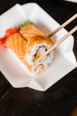 Holding philadelphia roll using chopstics for sushi. Roll with salmon, shrimp and mango. Japanese food delivery.