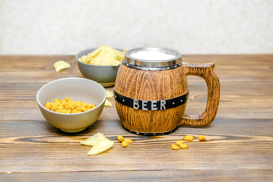 Brown Mug of beer with big foam and crispy snacks, chips, nuts in bowl on wooden rustic background close up. Alcohol cocktail, bar drink party concept