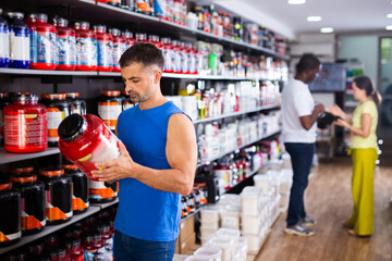 Interested sports man choosing food supplements in large assortment of sport nutrition store