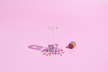 A bottle with scattered colored sequins of stars on a pink background. Minimalistic christmas new year concept