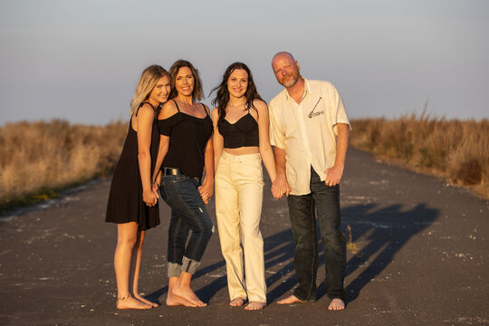 Happy family of four smiling and holding hands while standing barefoot on a country road outside. A Mother, Father and two daughters. 