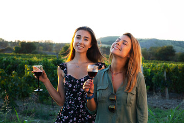 Beautiful girls tasting wine in a field near vineyard field. Celebrating successful harvest season. Couple having a romantic date. Rural tourism concept