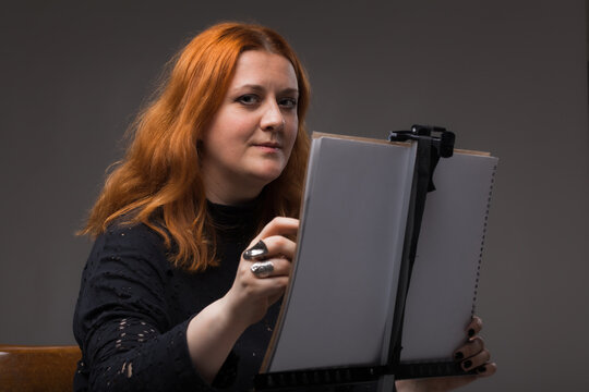Red hair woman painting. Portrait of an artist against gray background.