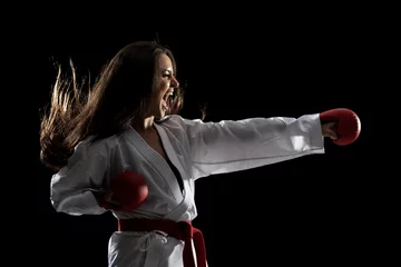 Fotobehang girl exercising karate punch and screaming against black background © Nikola Spasenoski