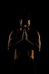 Obraz na płótnie Canvas Side lit muscular Caucasian man silhouette. Athlete praying against black background.