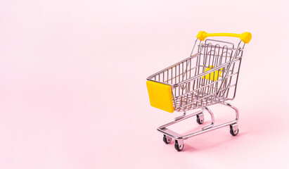 Miniature shopping cart isolated on a pink background