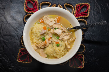 one bowl of steaming chicken and dumpling soup sitting on a colorful mat. a hearty meal full of chunks of meat, carrots, celery, onion and herbs. 